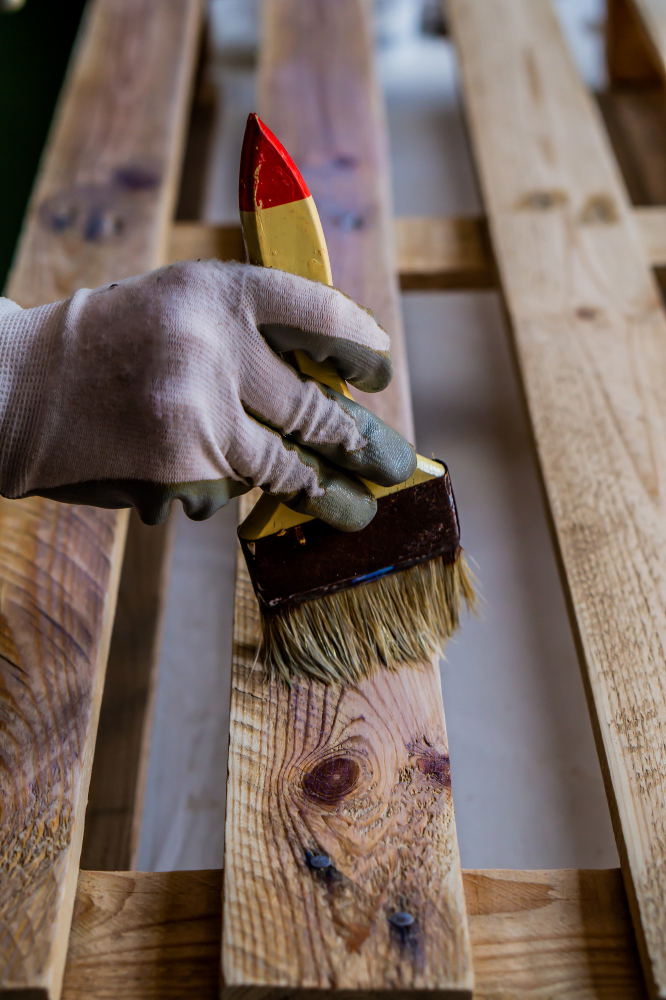 Persoon schildert houten pallet met kwast en beits voor bescherming en afwerking van hout